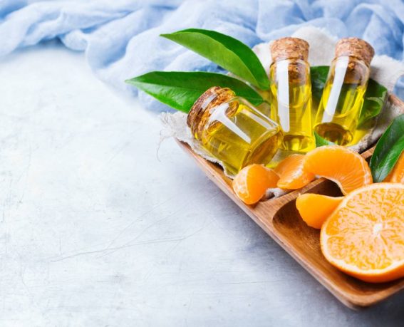 Health and beauty, still life concept. Organic essential tangerine, mandarin, clementine oil in a small glass jar with green leaves and orange fruit on a rustic table. Copy space background